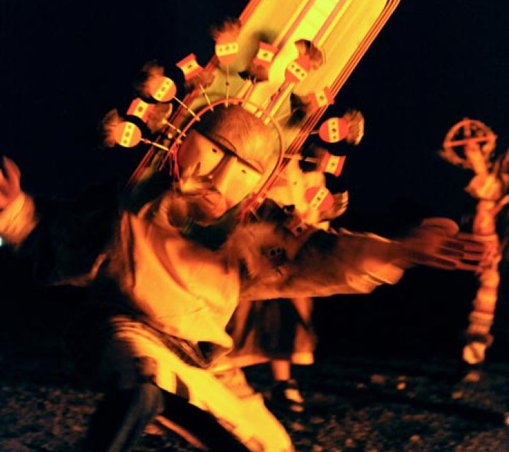 A masked dancercer performing by fire light.