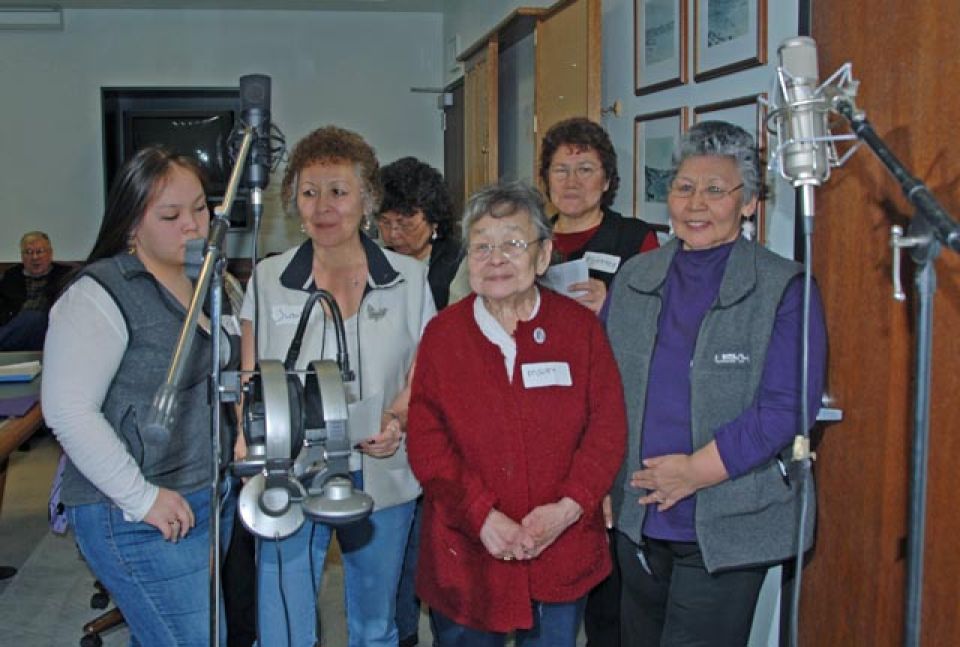 A group of Alutiiq ladies standing behind a microphone preparing to record a song.
